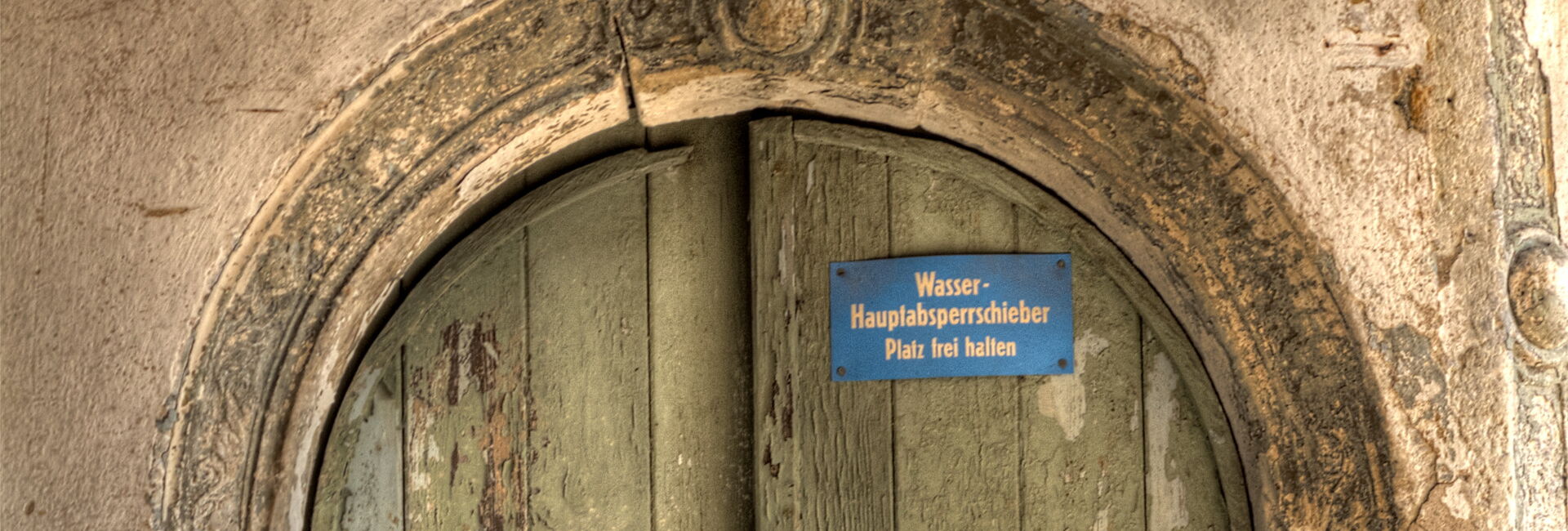 Sehr alte Holztür mit Stein und Schild.